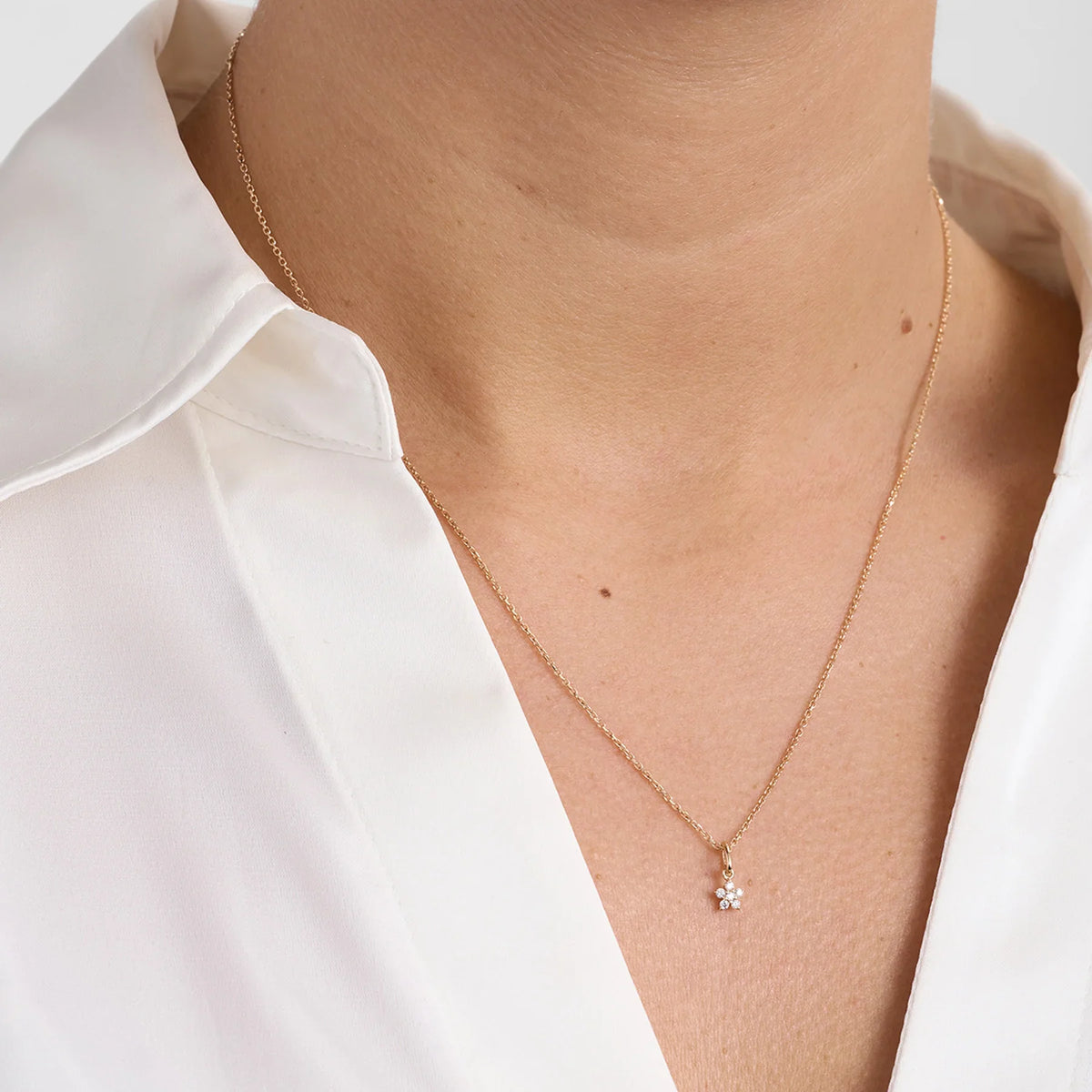 Goldene Halskette mit kleinem blütenförmigen Anhänger und Diamanten, Vorderseite am Modell