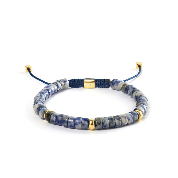 Alexander Lynggaard Armband Blue Spot Jasper Heishi geflochten 6 mm mit blauen und goldenen Details auf weißem Hintergrund. Modell B00222-1.