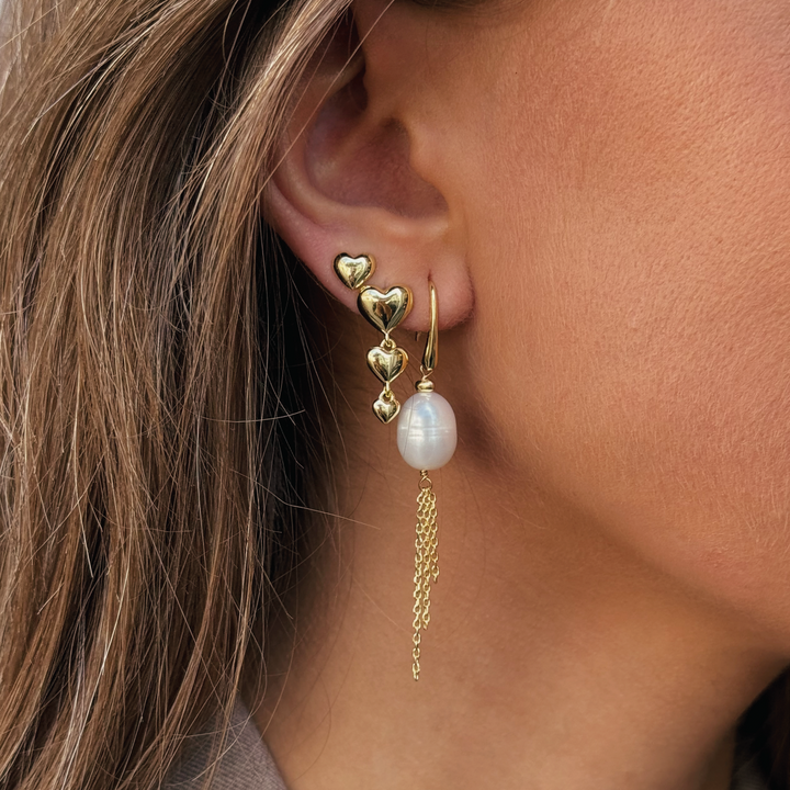 Aqua Dulce Karla And Me Long Earring zeigt einen eleganten goldenen Ohrring mit herzförmigen Details und Perlenanhänger, Modell 6422-2.