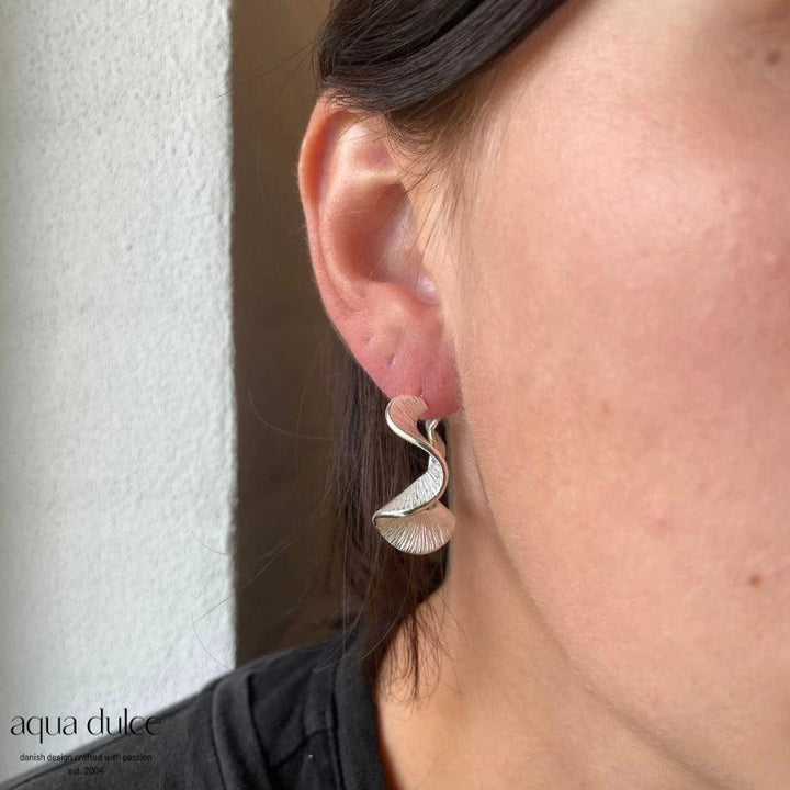 Aqua Dulce Rhumba Hoop Creole Silver am Ohr abgebildet, elegant gedrehter Creole in glänzendem Silber. Modell 5099-5099-2