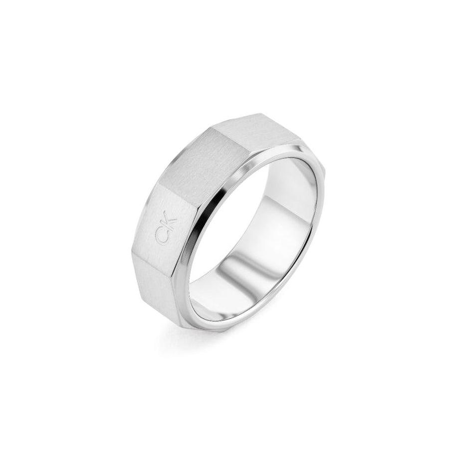 Der Calvin Klein Latch Ring zeigt einen breiten, silberfarbenen Herrenring aus gebürstetem Stahl mit facettiertem Rand. Modell 35000316-001.