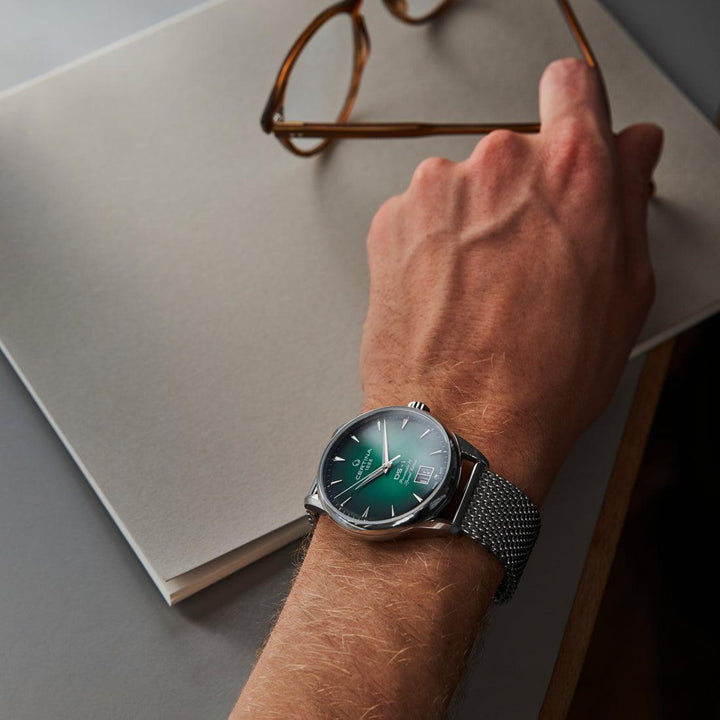 Certina DS-1 Big Date mit grünem Zifferblatt und Stahlgeflechtarmband, getragen am Handgelenk am Schreibtisch. Modell C0294261109160