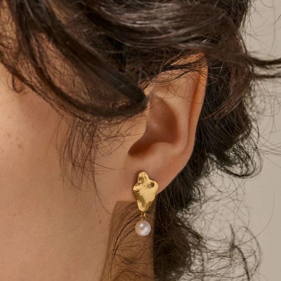 enamel-caia-small-earrings-e374gm erscheint am Ohr, mattgoldener Look mit hängender weißer Perle. Modell E374GM