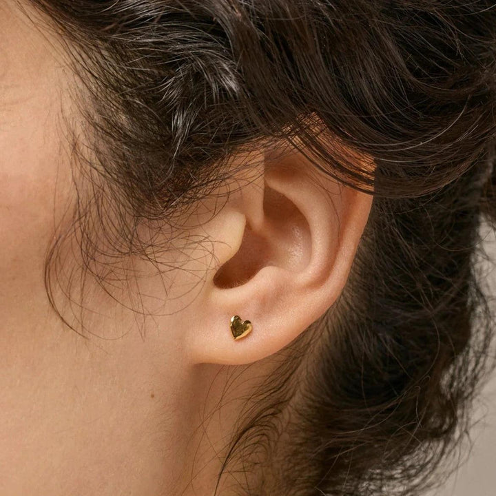 enamel Herzstecker Am Ohr sind vergoldete Herzstecker zu sehen, klein und goldglänzend. Modell E373GM