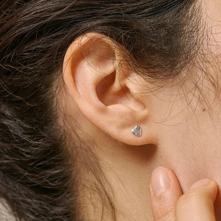 Enamel Heart Studs werden als silberfarbene Herzohrringe im Ohr des Models dargestellt, elegant und minimalistisch. Modell E373SM-E373SM-2