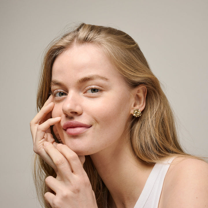 Enamel Großer Sonnenschein-Ohrstecker am Modell, goldene, sonnenförmige Ohrstecker im Ohr. Modell e421g-2