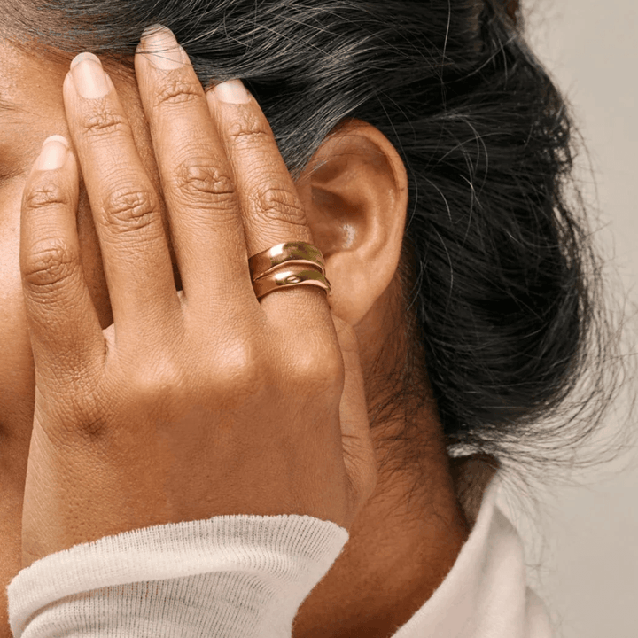 Enamel Sandra Statement Ring vergoldet erscheint an der Hand der Frau nahe am Ohr, glänzende goldene Oberfläche. Modell R92G-R92G-001.