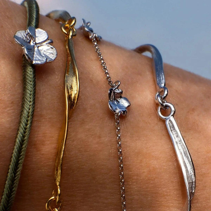 Flora Danica Am Handgelenk sind Kleeblatt-Seidenarmband in Olivsilber, olivgrüne Seidenschnur und Kleeblatt-Detail zu sehen. Modell907-FLC-SILK-OLIVE-S-001-2