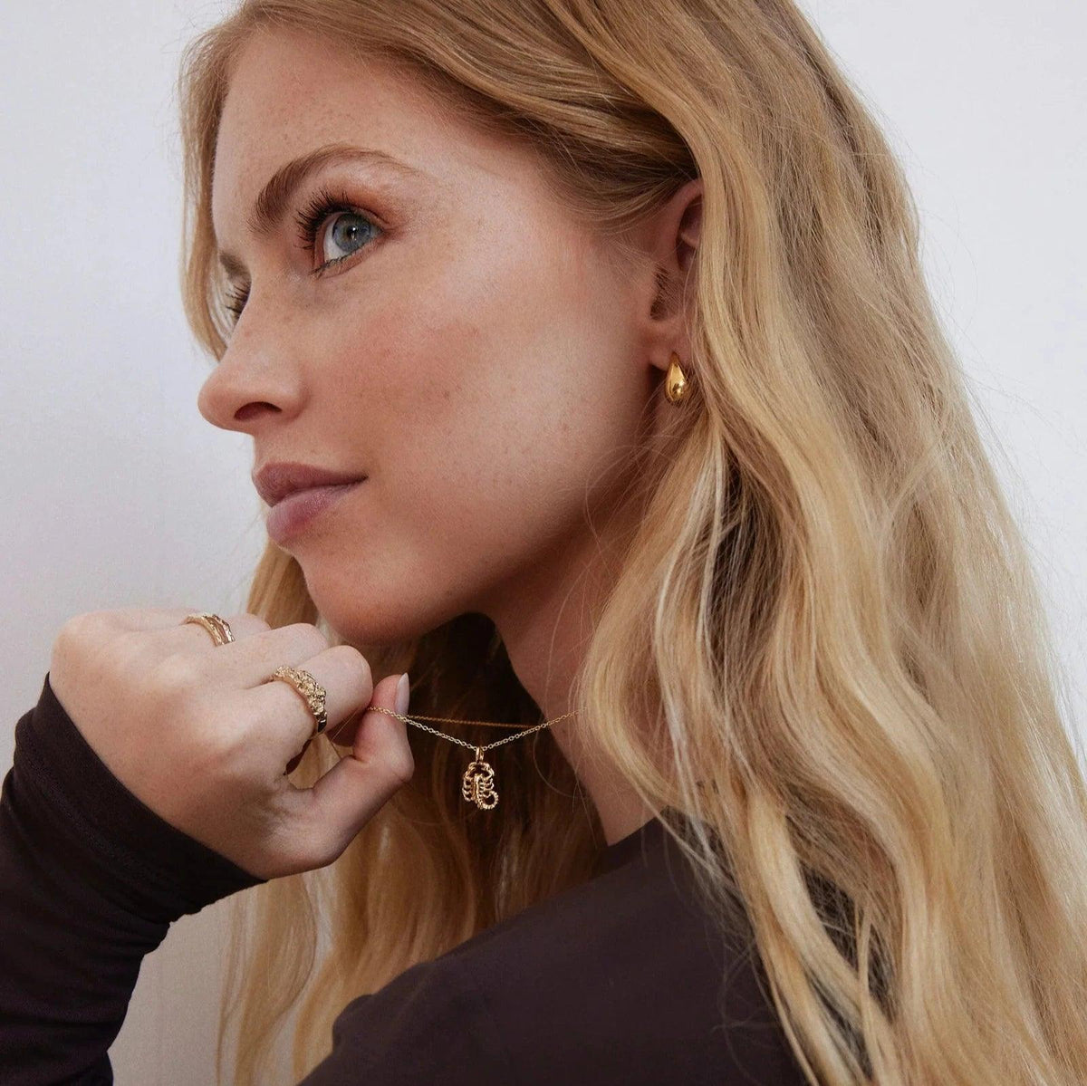 Jeberg I AM Zodiac-Halskette, vergoldetes Sternzeichen, getragen von einer Frau mit welligem, hellem Haar. Modell 42400-001.