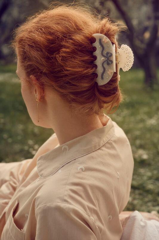 Maanesten-Desiree-Hair-Claw-Off-White ist in den gestylten roten Haaren der Frau in einer sonnigen Umgebung im Freien zu sehen. Modell 3973 – Einheitsgröße