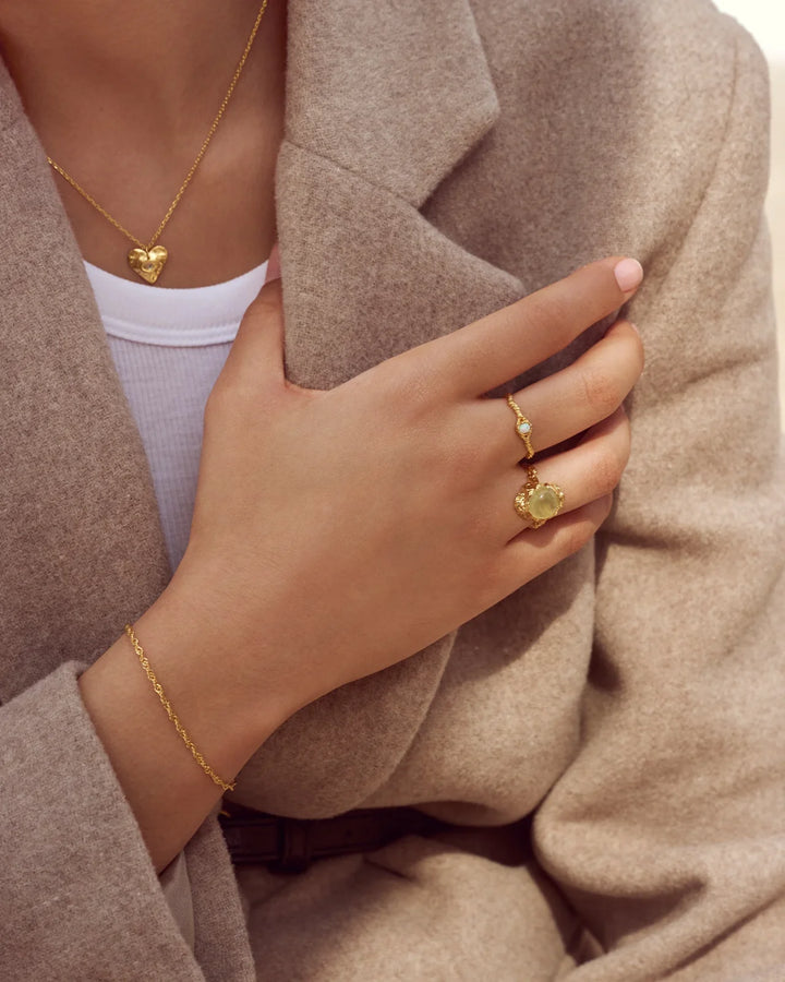 Der vergoldete Mondstein-Lisa-Ring ist an einer Hand mit beigem Mantel, goldener Farbe und einzigartiger Textur abgebildet. Modell 4745a-001-2.