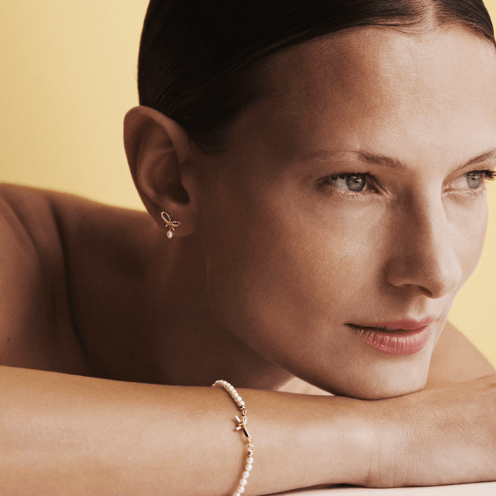 Mads Z Miss Butterfly Bow Pearl-Armband aus Gold und Diamanten, getragen von einer Frau vor hellem Hintergrund. Modell 1553030-2