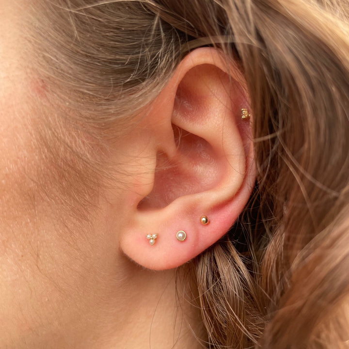 Maria Tash Pearl Trinity Stud ist im Ohr abgebildet, dezentes Gold und Perlen, elegantes Design. Modell xtrpe-yg-w3-001-2.