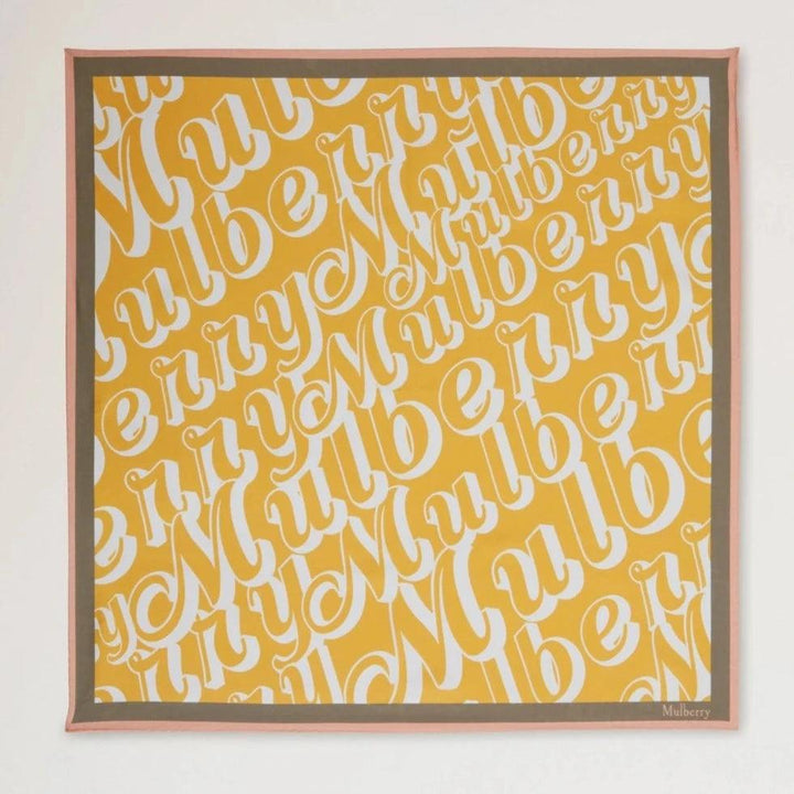 Mulberry Der Fantasy Logo Square Scarf zeigt einen gelben Schal mit Weiß Mulberry- Druck und rosa Rand. Modell VS4802027P504