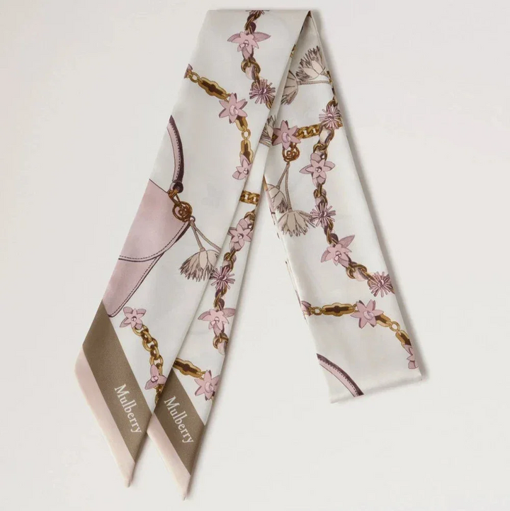 Mulberry Lana Bag and Chains Skinny Scarve Eggshell/Blossom Pink präsentiert einen schmalen Seidenschal mit rosa und goldenen Kettendetails. Modell VS4849115W569
