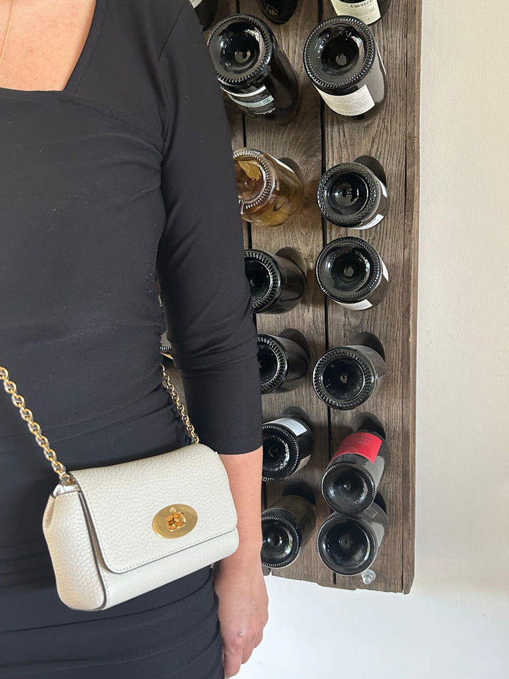 Mulberry Mini Lily Grobkörnige Kreide, getragen an der Umhängetasche einer Frau in schwarzer Kleidung, vor einem Weinregal. Modell rl7944736w160-2