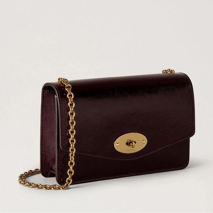Mulberry Klein Darley Deep Aubergine Patent zeigt eine kleine, glänzende Umhängetasche aus dunklem Aubergine-Leder mit goldenem Kettenriemen. Modell RL8922737V697