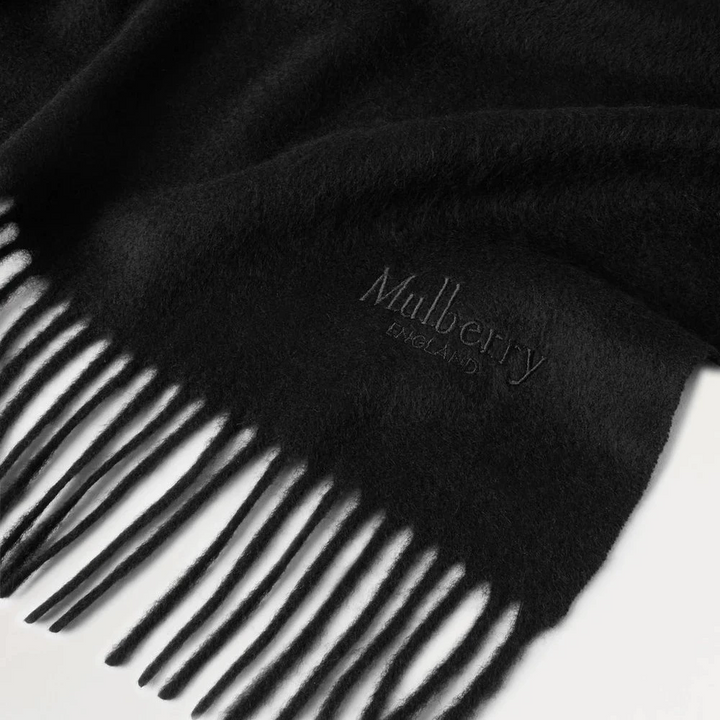 Mulberry Solid Merino Whool Scarf Black zeigt einen schwarzen Schal aus Merinowolle mit Fransen und dezentem Logo. Modell vs4240947a100