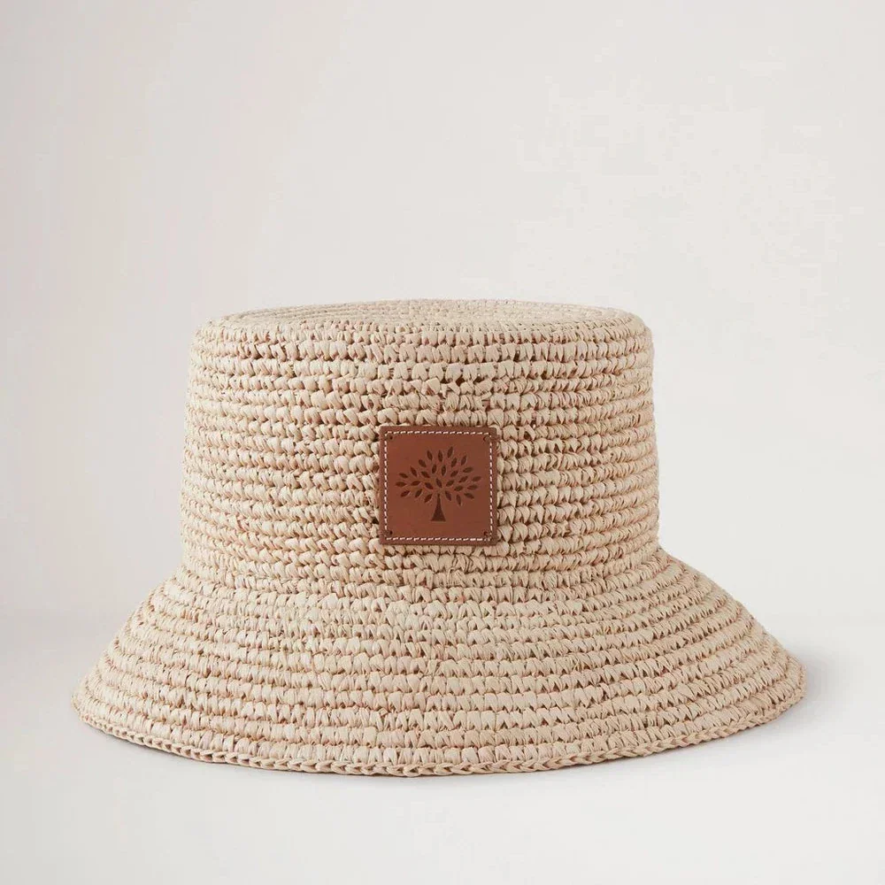 Mulberry Der Sommer-Raffia-Eimerhut präsentiert einen hellen, geflochtenen Bast-Sommerhut mit Lederdetail auf der Vorderseite. Modell VH4097807H120