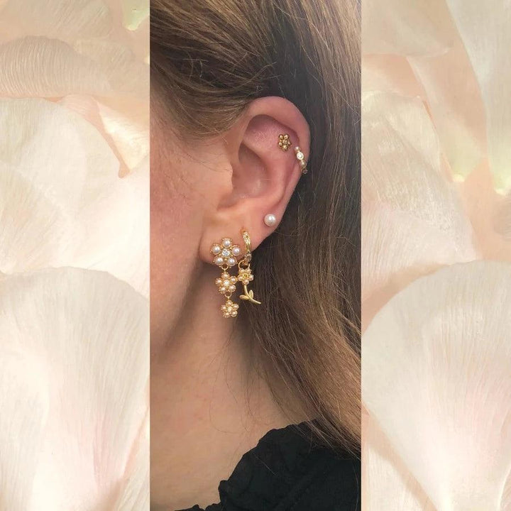 Poppy Stud zeigt elegante goldfarbene Ohrstecker mit Blumen und Perlendetails am Ohr, Modell FW2306-2.