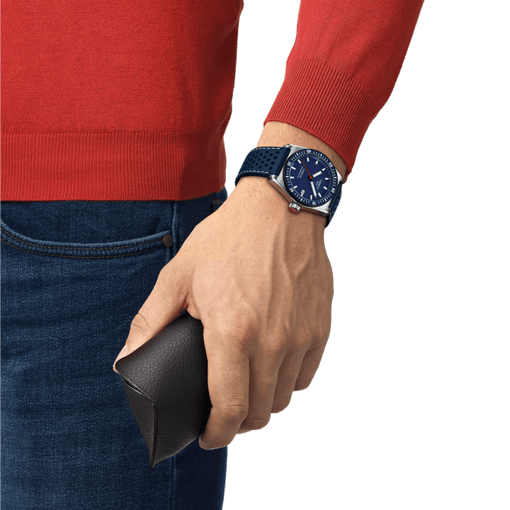 Tissot PR516 Powermatic 80 mit blauem Zifferblatt und perforiertem blauen Armband am Handgelenk, Modell T1494071604100.