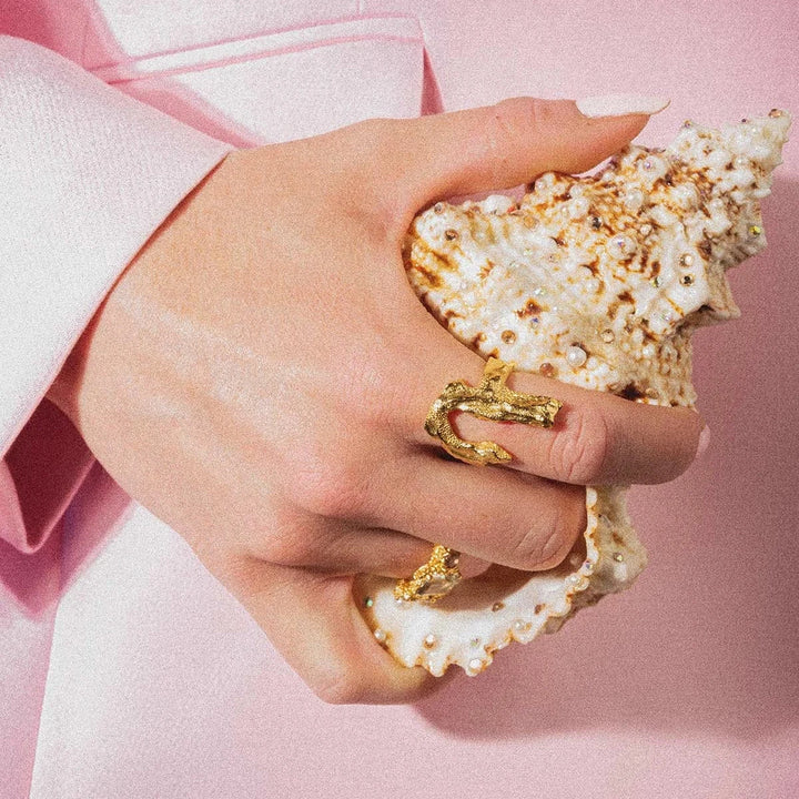 Abbildung zeigt den vergoldeten Vincent Bone-Ring, Detail eines goldfarbenen Rings vor einer Muschelschale. Modell vj229-urg-001