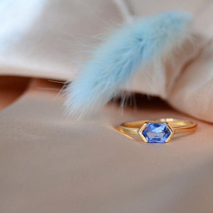 anpe-atelier-customized-ring-with-blue-saphir auf beigem Stoff, sechseckiger blauer Saphir in Gold. Modell27-blasafir-001-2