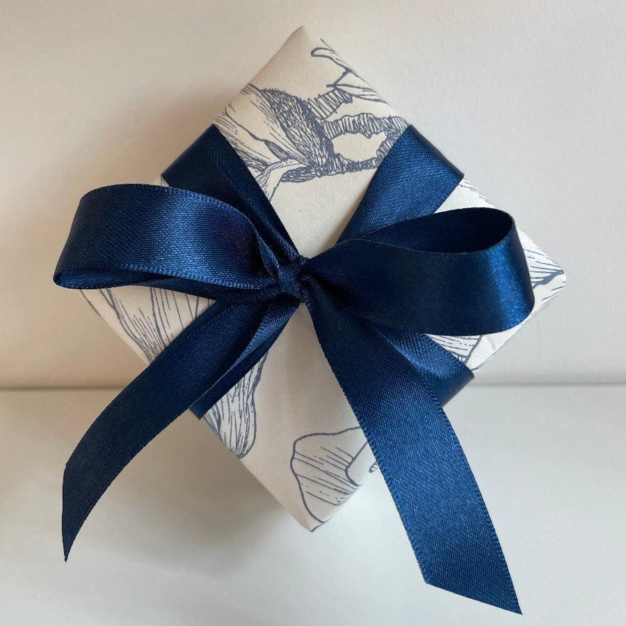 Kostenlose Verpackung, elegante Geschenkbox aus hellem Papier mit dunkelblauem Seidenband und dekorativem Motiv, Modell kostenlose Verpackung--1
