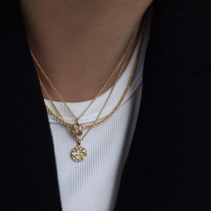 Die Halskette „I Am Gold Petite“ von Jeberg Jewellery wird mit einem runden, gemusterten Anhänger in Gold um den Hals getragen. Modell 40760-2