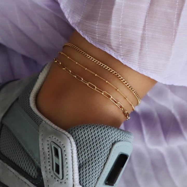 Das Jeberg Jewellery Saga Paner Fußkettchen aus vergoldetem Silber wird zusammen mit anderen Ketten am Knöchel präsentiert. Modell 4535-G-4535-G-2