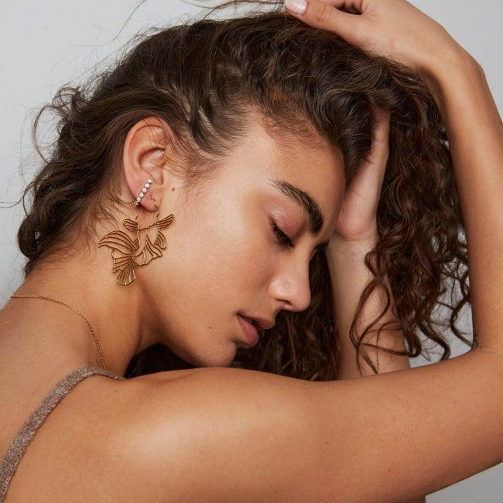 Vergoldete Koi-Creolen von Polar Jewelry erscheinen bei Frauen mit welligem Haar und eleganten goldfarbenen Ohrringen. Modell Koi-HP-GD-00101-2